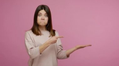 Şaşırmış esmer kadın avucunda boş bir yeri işaret ediyor ve ağzı açık bakıyor, şaşırmış yüz ifadesi, reklam alanında reklam metni gösteriyor, elinde kopya alanı var. Stüdyoda çekim izole edildi