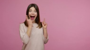Şaşırmış esmer kadın boş yeri işaret ediyor ve başparmaklarını kaldırıyor, ağzı açık bakıyor, hayret verici bir ifade, reklam alanını gösteriyor, reklam metinleri için, kopyalama alanı için. Stüdyoda çekim izole edildi