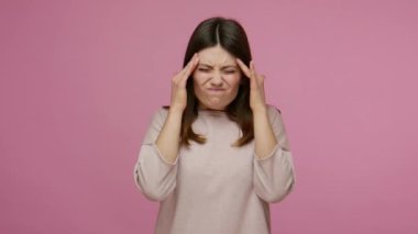 Depresyondaki genç esmer kadın şiddetli migren ağrısı çekiyor, baş şakaklarını ovuyor ve baş ağrısından çatık kaşlarını çatıyor, sıkıntıların gerginliğini hissediyor. Pembe arka planda kapalı stüdyo çekimleri