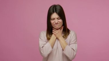 Grip virüsü belirtileri. Genç esmer kadın şiddetli acı çekiyor, boyna dokunuyor ve boğaz ağrısı, tiroid bozukluğu, gırtlak iltihabı yüzünden kaşlarını çatıyor. Pembe arka planda kapalı stüdyo çekimleri