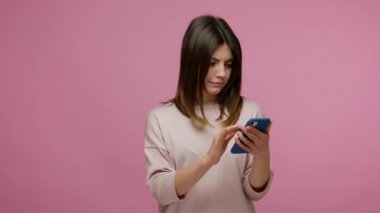 Güzel esmer, genç bir kadın internet günlüğünü akıllı telefondan çeviriyor, sosyal ağda fotoğraflar izliyor ve mobil uygulama kullanarak hayretler içinde kaldığını ifade ediyor. Pembe arka planda kapalı stüdyo çekimleri