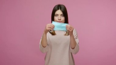 Kamerayı gösteren ve yüzüne hijyenik tıbbi maske takan bir kadın solunum hastalıklarını ve koronavirüsü önlemek için nasıl filtre takılacağını gösteriyor. Pembe arka planda kapalı stüdyo çekimleri