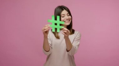 Güzel kız, güzellik blogcusu hashtag sembolü gösteriyor ve neşeli bir şekilde gülümsüyor, foruma katılmayı öneriyor, etiketli mesajı takip ediyor, popüler blog fikri. Stüdyo çekimi pembe arkaplanda izole edildi
