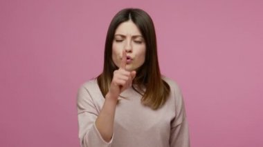 Shh, sessiz ol! Endişeli esmer genç kadın sessiz kalmak istiyor ve sır tutmak için parmaklarını dudaklarında tutarak gizli bilgiler vermiyor. Pembe arka planda kapalı stüdyo çekimleri