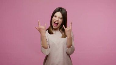 Evet, bu delilik! Kaygısız esmer kadının rock 'n roll işareti göstermesi ve sanki hard rock festivalindeymiş gibi kükremesi şeytan boynuzları sallaması. Stüdyo çekimi pembe arkaplanda izole edildi