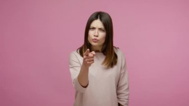 Hey sen! Katı, hoşnutsuz esmer kadın kamerayı suçluyor ve işaret ediyor, hata için suçluyor, ciddi patronluk taslayan bir ifadeyle azarlıyor. Pembe arka planda kapalı stüdyo çekimleri