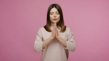 Huzurlu zihin, meditasyon. Güzel sakin esmer kadın namaste ile ayakta duruyor, dua eden el hareketi ve rahatlamak için gözlerini kapatıyor, zihinsel yoga alıştırması yapıyor. Pembe arka planda kapalı stüdyo çekimleri