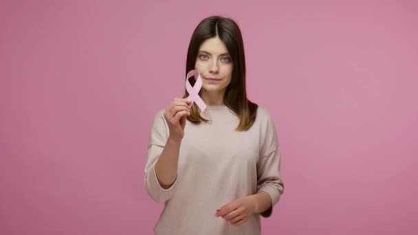 善良的黑发女人 带着粉色带子 是乳腺癌意识的象征 是预防癌症的建议和警告 是女性健康诊断的标志 在粉红背景下隔离的室内拍摄 — 图库视频影像