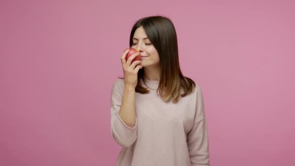 健康的な幸せなブルネットの女性は新鮮な赤いリンゴの匂いを楽しんで ジェスチャー おいしいビタミンフルーツ 低カロリーの自然食品のような親指を示す ピンクの背景に隔離された屋内スタジオで — ストック動画