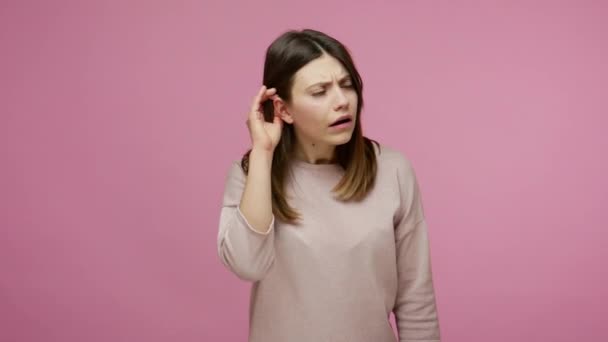 布鲁内特妇女在很小的时候就亲耳听着谈话 表示怀疑 对所听到的信息感到不确定 有听力问题和耳聋 室内拍摄 粉红背景 — 图库视频影像