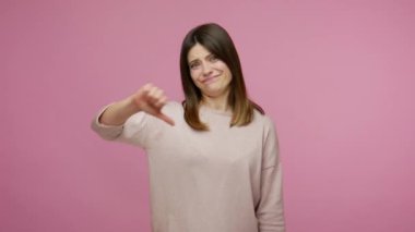 Tatminsiz esmer kadının hoşnutsuzluğu ve hoşnutsuzluğu baş parmaklarını göstermesi, jestten hoşlanmaması, eleştirmesi ve onaylamamasını eleştirmesi, korkunç bir geri bildirim. Pembe arka planda kapalı stüdyo çekimleri