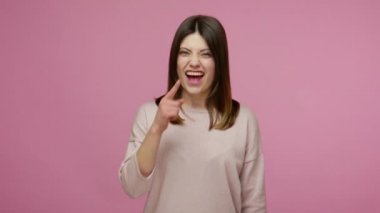 Komik bir suratı olan kaygısız esmer kadın, gülmek ve sümük çıkarmak, eğlenmek için pis burnunu delmek, şaka yapmak. Pembe arka planda kapalı stüdyo çekimleri