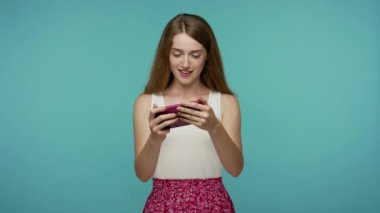 Yazlık elbiseli güzel bir kız cep telefonuyla video oyunu oynuyor, mobil uygulamayı sürücü simülatörüyle kullanıyor, boş zamanlarını internet eğlencesine harcıyor. Mavi arka planda kapalı stüdyo çekimleri