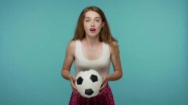 Güzel bir kız futbol fanatiği elinde futbol topu tutuyor ve maç izlemek için can atıyor. Gol kazanma umuduyla, sevinç ve zafer için bağırıyor. Mavi arka planda kapalı stüdyo çekimleri