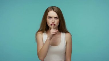Shh, sessiz ol! Çok ciddi bir kız sakin kalmak istiyor, sessiz kalmak ya da gizlilik istiyor parmakları dudağında, gizemli gizli bilgiler. Mavi arka planda kapalı stüdyo çekimleri