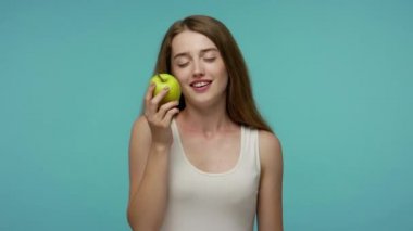 İnce, mutlu, yaz elbisesi giymiş, lezzetli elmalar yiyen taze meyve, vitamin yiyeceği, sağlıklı beslenme ve vejetaryen yaşam tarzının tadını çıkaran bir kız. Mavi arka planda kapalı stüdyo çekimleri