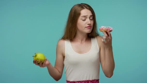 Szczupła Piękna Dziewczyna Pachnąca Pączkiem Gryzącym Jabłkiem Dokonując Wyboru Między — Wideo stockowe
