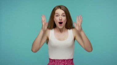 Piyangoda inanılmaz bir galibiyet elde eden mutlu kız ellerini kaldırarak zafer için tezahürat yapıyor ağzını şaşkınlıkla açıyor, şaşkın şaşkın bakıyor. Stüdyo çekimi mavi arkaplanda izole edildi