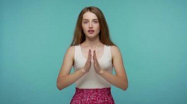 Sakin ol, sakin ol. Güzel bir yaz elbisesi içinde, gözleri kapalı dua ederken el ele tutuşan, konsantre düşüncelerle meditasyon yapan, iç dengeli bir kız. Stüdyo çekimi mavi arkaplanda izole edildi