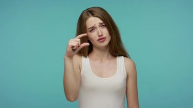 Hayal kırıklığına uğramış, acınası bir ifadeyle kameraya bakan, küçük boyutta, düşük ölçekli şüpheci tavırları olan tatlı, pozitif bir kız. Stüdyo çekimi mavi arkaplanda izole edildi