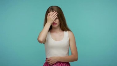 Omg, facepalm, hepsi benim hatam! Üzüntülü kız, yüzü başıyla örtülmüş ve hayır diyor, kendini suçluyor, üzgün, utangaç ve mahcup hissediyor. Stüdyo çekimi mavi arkaplanda izole edildi