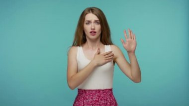 Yemin ederim! Yazlık elbiseli, elini kaldıran, göğsüne dokunan, samimi bir söz veren, sorumluluk sahibi bir ifadeyle yemin eden endişeli, dürüst bir kız. Mavi arka planda kapalı stüdyo çekimleri