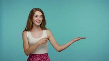 Elimdeki ürüne bak! Yazlık elbiseli neşeli kız avucundaki reklam alanına bakıyor, reklam metni ve reklam için boş bir yer gösteriyor. Stüdyo çekimi mavi arkaplanda izole edildi