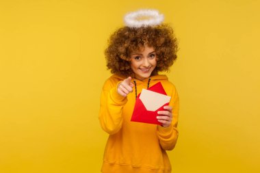 Aşk mesajı. Güzel kıvırcık saçlı melek gibi bir kadının portresi. Elinde mektup zarfıyla kamerayı göstererek neşeli bir şekilde gülümsüyor. Sarı arka planda izole edilmiş kapalı stüdyo çekimi