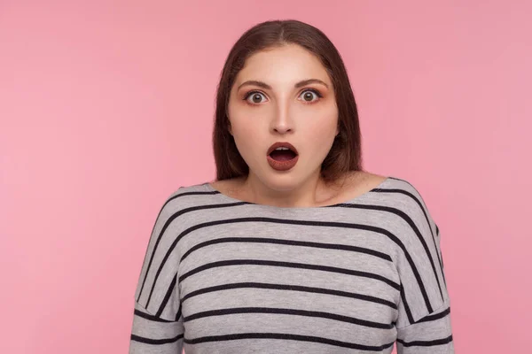 Oh my god, wow! Portrait of surprised woman in striped sweatshirt standing with open mouth, expressing amazement, astonished by unbelievable shocking news. studio shot isolated on pink background