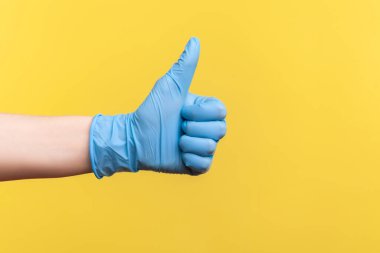 Profil yan görüntüsü, insan elinin mavi cerrahi eldivenli hali. Onaylandı ya da onaylandı. İçerde, stüdyoda, sarı arka planda izole edilmiş..