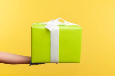 Profil yan görüntüsü, elinde hediye kutusu olan mavi eldivenli insan eli. Paylaşım, verme veya teslim etme kavramı. İçerde, stüdyoda, sarı arka planda izole edilmiş..