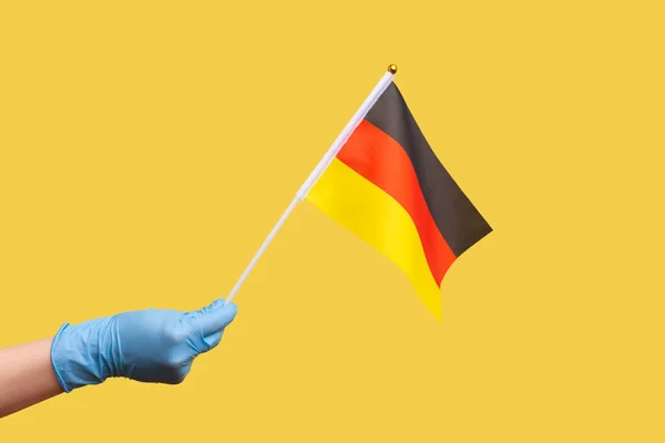 人手在蓝色手术手套中的侧视特写 手持德国国旗 德国日 10月3日 工作室拍摄 隔离在黄色背景下 — 图库照片