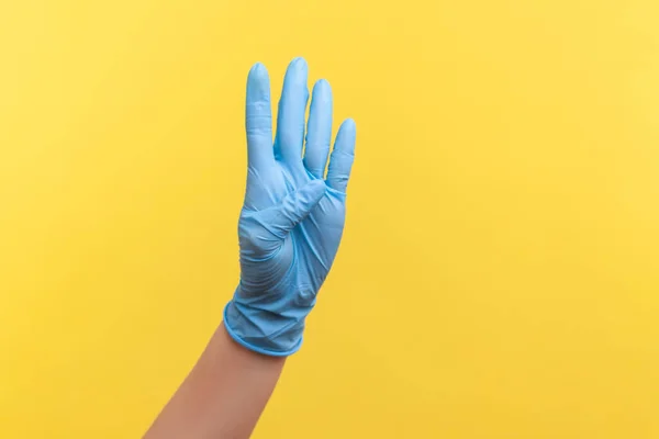 手で4番目を示す青い外科用手袋の人間の手のプロフィール側のビューの閉鎖 黄色の背景に隔離された屋内スタジオでの撮影 — ストック写真