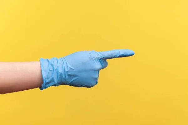 指で何かを示すか または指して青い外科用手袋で人間の手のプロフィール側のビューを閉じます 黄色の背景に隔離された屋内スタジオでの撮影 — ストック写真