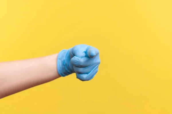 Profile side view closeup of human hand in blue surgical gloves showing or pointing at camera. indoor, studio shot, isolated on yellow background.
