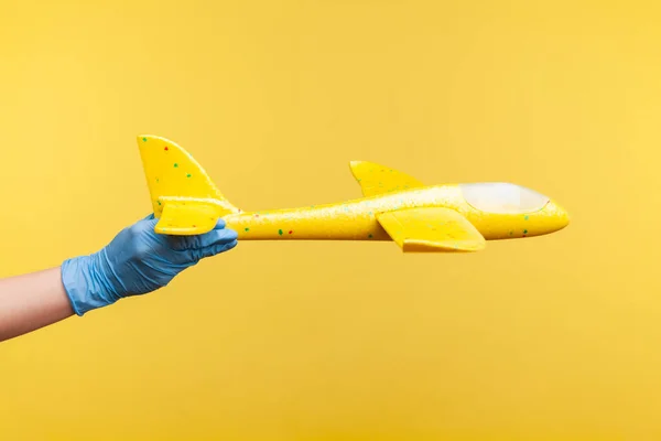 黄色の飛行機モデルを保持青い外科手袋の人間の手のプロフィール側のビューの閉鎖 黄色の背景に隔離された屋内スタジオでの撮影 — ストック写真