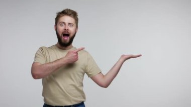Şaşırmış sakallı adam avucunda boş bir alan tutuyor ve ağzı açık bakıyor. Şaşırmış bir şekilde, reklam ürünleri için boş bir yer gösteriyor. Stüdyo çekimi gri arkaplanda izole edildi