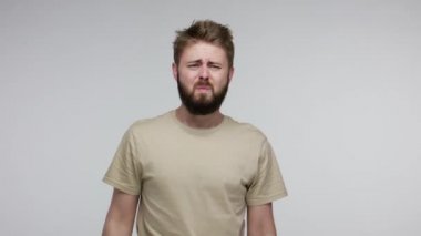 Diş sorunları. Yaralı yanağa dokunan sağlıksız sakallı adam acıdan çatık kaşlı diş ağrısı, çürük veya diş eti iltihabı belirtileri, diş eti hastalığı. Gri arka planda kapalı stüdyo çekimi