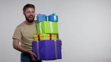 Mutlu sakallı adam doğum gününü kutluyor, yürüyor ve bir sürü hediye kutusu taşıyor, neşeli bir gülümsemeyle kameraya bakıyor, tatilin tadını çıkarıyor. Gri arka planda kapalı stüdyo çekimi