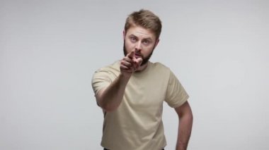 Hey sen! Kızgın sakallı adam suçluyu fark ediyor ve kamerayı işaret ediyor. Katı kızgın bakıyor, davranışlarından memnun değil, sorunlarla suçluyor. Gri arka planda kapalı stüdyo çekimi