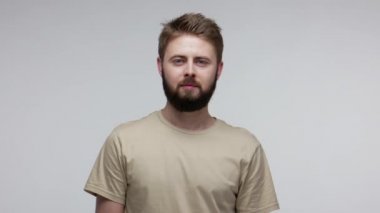 Ciddi yakışıklı, sakallı bir adam kameraya bakıyor. Gülümsemiyor, konsantre olmamış, sakin, kendine güveni tam, içten bir yüz ifadesi olan biri. Gri arka planda kapalı stüdyo çekimi