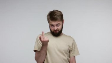 Çılgın holigan sakallı adam orta parmaklarını gösteriyor, kaba bir saygısızlıkla protesto ediyor, iletişimi reddediyor. Gri arka planda kapalı stüdyo çekimi