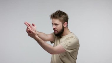 Sakallı adam hedefini arıyor, işaret parmağı işareti yapıyor ve seni kameraya çekiyor, nişan almak için silahla öldürüyor, iyi atıştı. Gri arka planda kapalı stüdyo çekimi