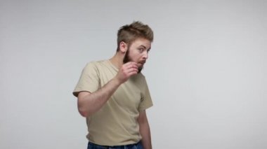 Meraklı, meraklı, sakallı, parmaklarının arasından meraklı gözlerle bakan, yasaklı sırları dikkatle izleyen, ürkek, ürkek bakışlı bir adam. Gri arka planda kapalı stüdyo çekimi