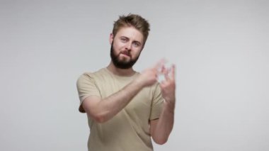 Tişörtlü modaya uygun sakallı adam hashtag jesti yapıyor dişlek gülüşlü kameraya bakıyor, popüler internet içeriğini etiketliyor, viral mesajla haşhaş işareti yapıyor. Gri arka planda kapalı stüdyo çekimi