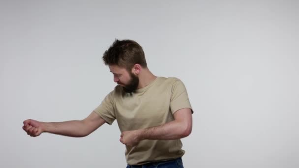 一个留着胡子的家伙 穿着T恤 非常努力地拉绳子 假装拖着沉重的物体 努力地运用他所有的力量肌肉 在灰色背景下隔离的室内拍摄 — 图库视频影像