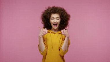 Kapüşonlu kapüşonlu neşeli afro saçlı kız saç stili ve hareketler gibi güçlü bir şekilde başparmaklarını kaldırıyor, mükemmel sonuçtan memnun hissediyordu. Stüdyo çekimi izole, pembe arkaplan