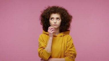 Kafası karışık afro saçlı, kapüşonlu, çenesine dokunan, çözümü düşünürken başını kaşıyan zor bir seçim hakkında şüpheleri olan düşünceli bir kız. Pembe arka planda kapalı stüdyo çekimleri