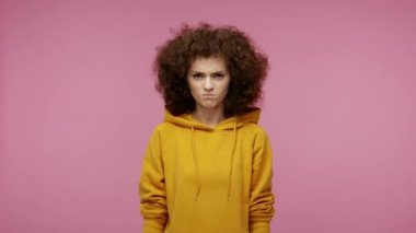 Kapüşonlu, kızgın, afro saçlı kız ellerini kaldırıyor ve çılgınca kükreyen, nefret dolu saldırganlık dolu, sinirlenmiş bir şekilde bağırıyor. Pembe arka planda kapalı stüdyo çekimleri