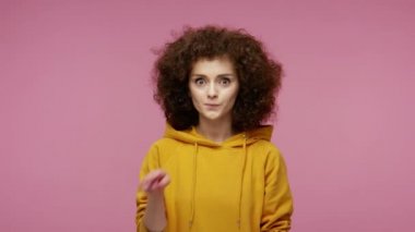 Lütfen, sessiz olun! Kapüşonlu kapüşonlu, dudak hareketleriyle gülümseyen afro saçlı kız sessiz kalmak, komplo kurmak ve gizem konseptini korumak istiyor. Pembe arka planda kapalı stüdyo çekimleri